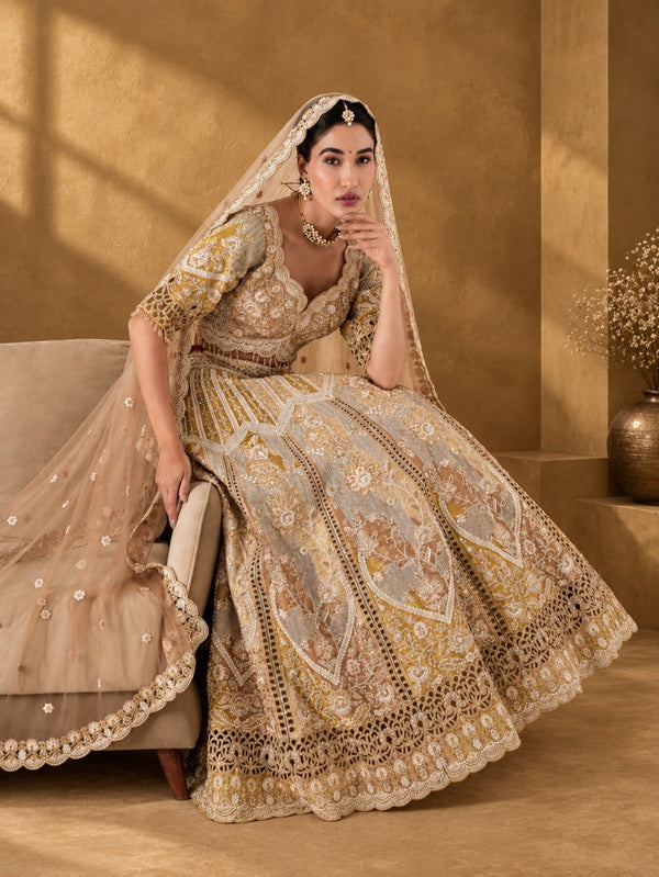 Model seated on a sofa in an antique gold cutwork lehenga with a sheer scalloped-edge dupatta