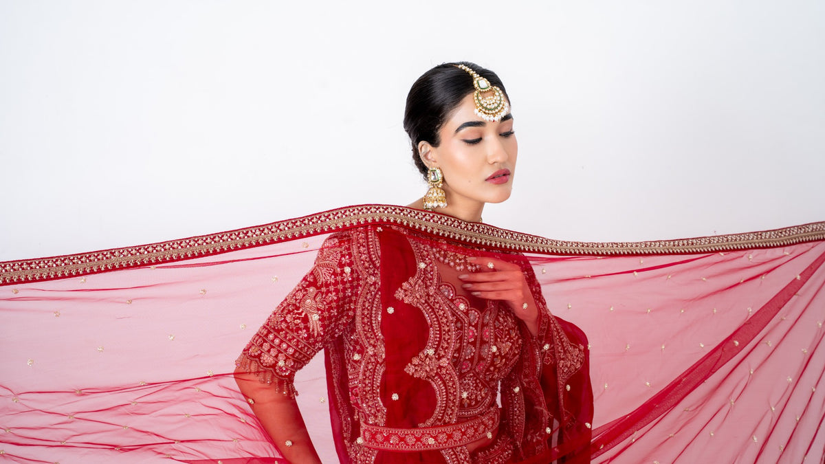 Bride in a red lehenga with a sheer embroidered dupatta sweeping across the frame