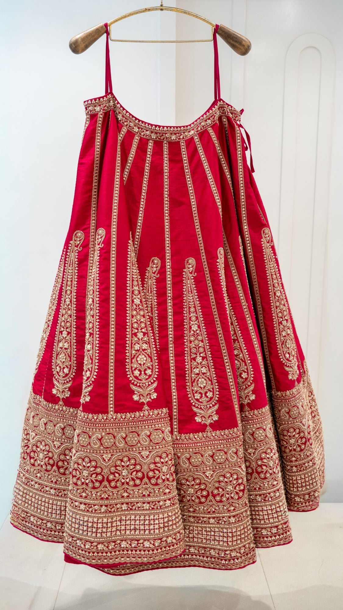 Red lehenga skirt with gold paisley embroidery on a brass hanger
