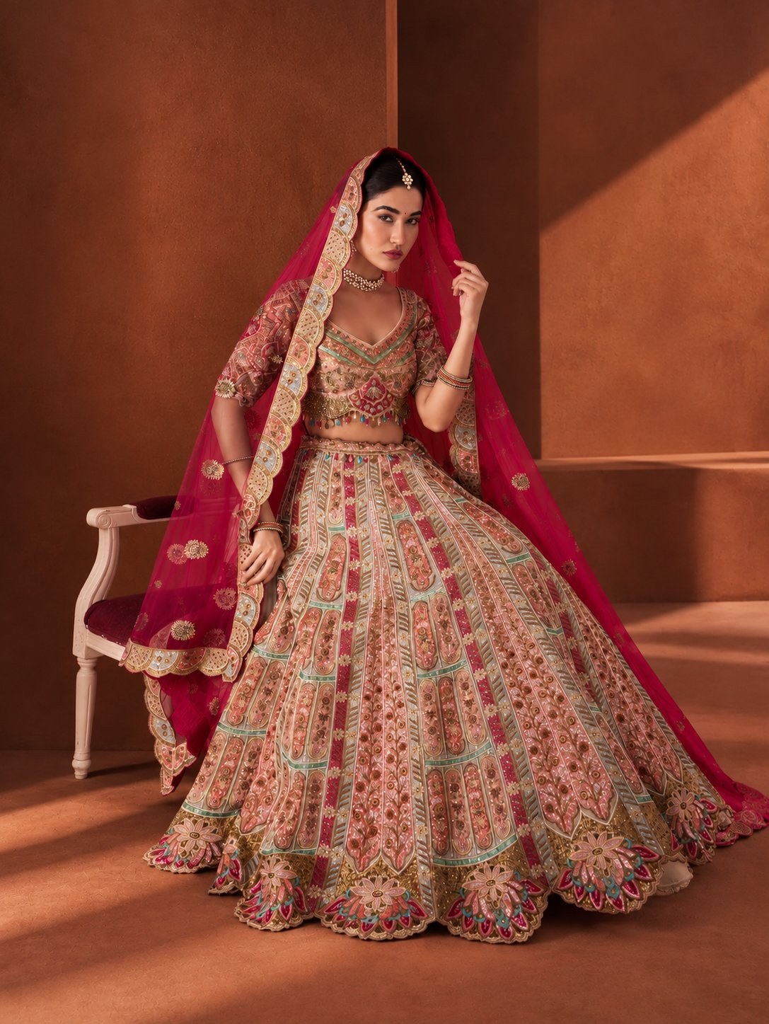 Bride seated in a rose multicolour embroidered bridal lehenga with a red scalloped dupatta